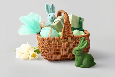 Boyanmış Paskalya yumurtaları, oyuncak tavşanları, hediye kutuları ve beyaz arka planı olan hasır sepet.
