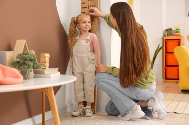 Genç anne, evdeki ahşap stadyumun yanında kızının boyunu ölçüyor.