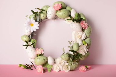 Güzel Paskalya çelengi pembe ve beyaz arka planda çiçekler ve yumurtalarla süslenmiş.