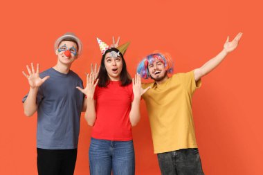 Turuncu arka planda kağıt balıkla kılık değiştirmiş genç şok olmuş arkadaşlar. 1 Nisan kutlamaları