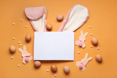 Tavşan kulakları, Paskalya yumurtaları, kağıt tavşanlar ve turuncu arka planda boş bir kart. Üst görünüm