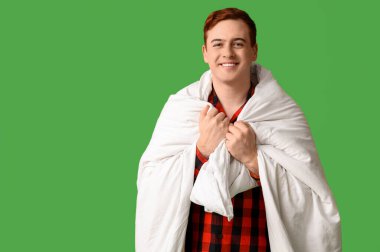 Yeşil arka planda battaniyeye sarılı yakışıklı genç adam.