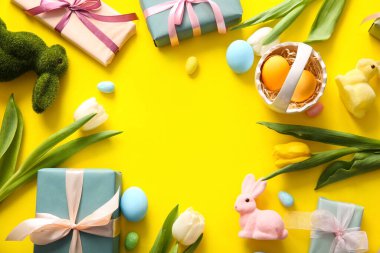 Paskalya yumurtaları, lale çiçekleri hediye kutuları ve sarı arka planda tavşanlardan yapılmış çerçeveler.