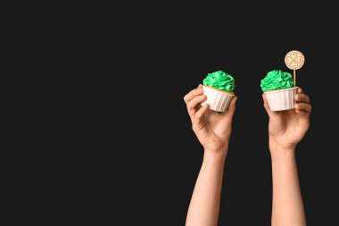 Siyah arka planda Aziz Patrick Günü için lezzetli kekleri olan kadın eller.