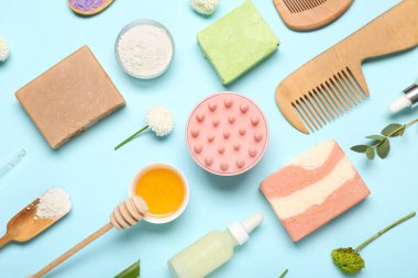 Saç derisi masaj aletleri, şampuanlar, farklı cilt ürünleri ve mavi arka planda çiçekler.