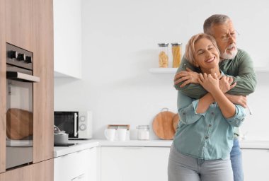 Olgun bir çift mutfakta sarılıyor.