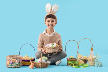 Mavi arka planda Paskalya sepetleriyle tavşan kulağı takan şirin bir çocuk.
