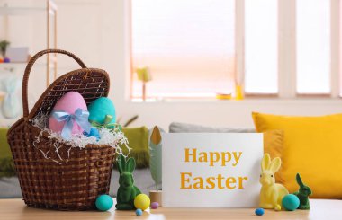Paskalya yumurtalı sepet, oyuncak tavşanlar ve oturma odasındaki masada tebrik kartı.