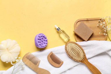 Saç derisi masaj aleti, şampuan barı, fırçalar ve sarı arka planda banyo malzemeleri.