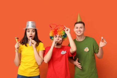 Turuncu arka planda kağıt balıklar ve ıslıklarla kılık değiştirmiş genç şok olmuş arkadaşlar. 1 Nisan kutlamaları