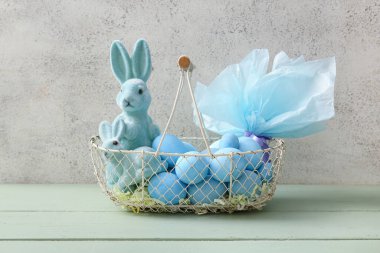 İçinde boyanmış Paskalya yumurtaları, oyuncak tavşanlar ve yeşil ahşap masal üzerine hediye çantası olan sepet.