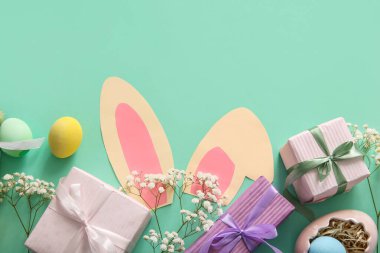 Paskalya yumurtaları, hediye kutularıyla çiçekler ve turkuaz arka planda kağıt tavşan kulakları.