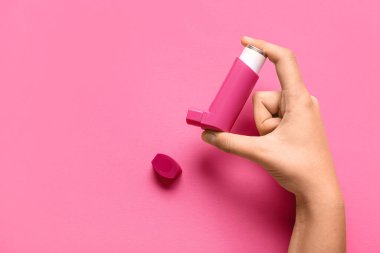 Pembe arka planda astım spreyi olan bir çocuk eli.