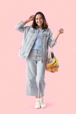Pembe arka planda bir torba taze sebzeli genç kadın.