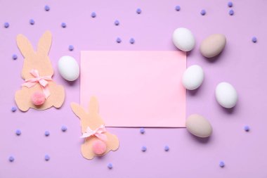 Paskalya yumurtaları, keçeli tavşanlar ve leylak arka planda boş tebrik kartları.