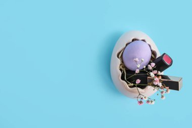 Paskalya yumurtası şeklinde bir sepet. Mavi arka planda ruj ve çiçekler var.