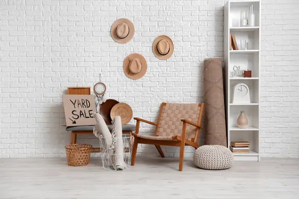 İstenmeyen bir çok şey ve kartondan yazılı YARD satışı odadaki beyaz tuğla duvarın yanında.