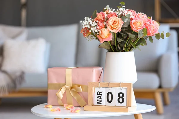 Calendar with date of International Women\'s Day, flowers and gift box on table in living room, closeup