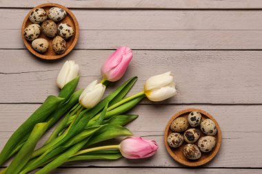 Gri ahşap arka planda Paskalya yumurtaları olan güzel lale çiçekleri ve kaseler.