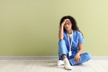 Stresli kadın Afro-Amerikan stajyer doktor yeşil duvarın yanında oturuyor.