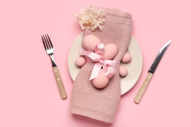 Paskalya yumurtaları, peçete ve pembe arka planda çatal bıçak seti olan şık bir masa.