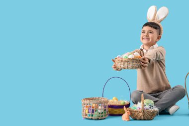 Mavi arka planda Paskalya sepetleriyle tavşan kulağı takan şirin bir çocuk.