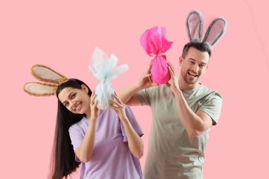 Pembe arka planda Paskalya hediyesi yumurtaları olan tavşan kulaklı mutlu çift.