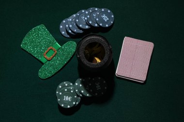 Poker fişleri, kartlar, bozuk paralar ve koyu yeşil arka planda leprikon şapkası. Aziz Patrick Günü kutlaması