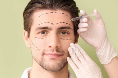 İşaretli yüzü olan genç adam yeşil arka planda enjeksiyon alıyor, yakın plan. Estetik ameliyat konsepti