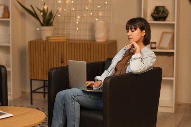 Akşamları siyah koltukta dizüstü bilgisayar kullanan genç bir kadın.