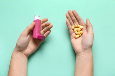 Astım spreyli çocuk elleri ve turkuaz arka planda haplar.