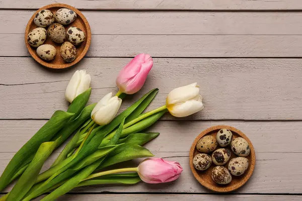 Gri ahşap arka planda Paskalya yumurtaları olan güzel lale çiçekleri ve kaseler.
