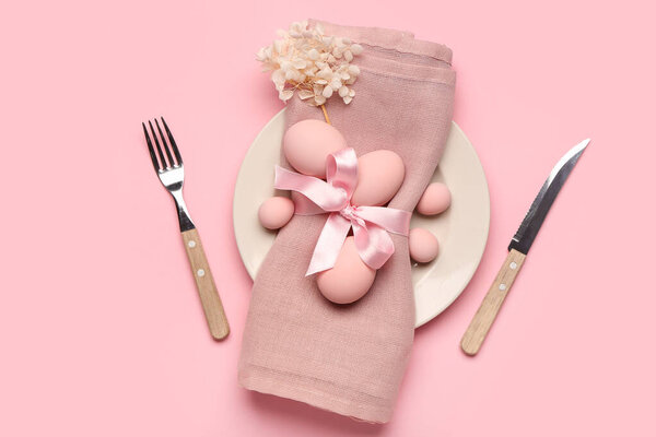 Стильная сервировка стола с пасхальными яйцами, салфеткой и столовыми приборами на розовом фоне