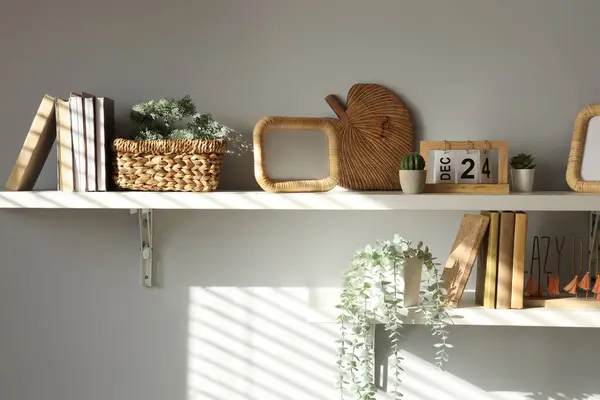 Shelves with frame, books and plants on light wall in dining room