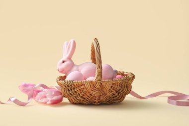Boyanmış Paskalya yumurtaları, oyuncak tavşancık ve sarı arka planda lale çiçekleri olan hasır sepet.