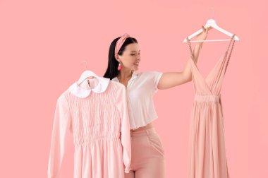 Güzel genç bir kadın pembe arka planda elbise seçiyor.