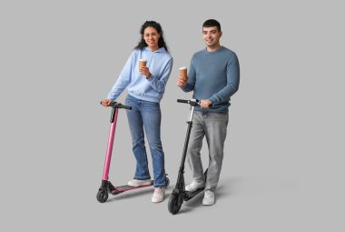 Modern elektrikli scooterları ve gri arka planda kağıt kahve fincanları olan güzel bir çift.