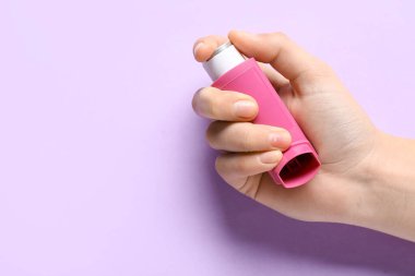 Leylak arka planında astım spreyi olan bir çocuk eli.