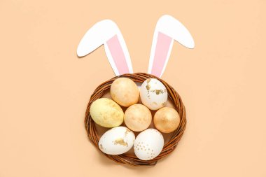 Boyanmış Paskalya yumurtaları ve bej arka planda kağıt tavşan kulakları olan bir yuva.