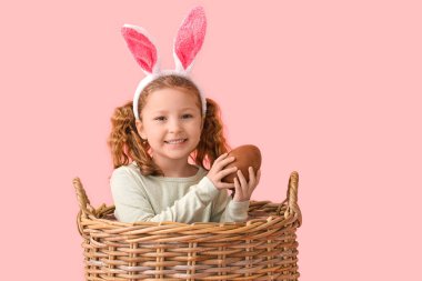 Paskalya yumurtası sepetinde pembe arka planda küçük tatlı bir kız.