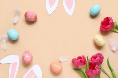 Lale çiçeklerinden yapılmış çerçeve, Paskalya yumurtaları ve bej arka planda kağıt tavşan kulakları.