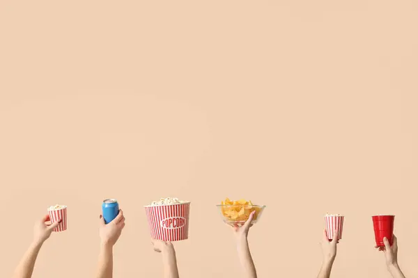 Hands holding popcorn, potato chips and drinks on beige background