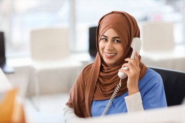 Kadın Müslüman stajyer klinikteki resepsiyonda telefonla konuşuyor.