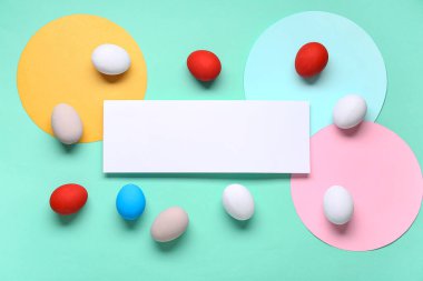 Renkli Paskalya yumurtaları ve turkuaz arka planda boş tebrik kartı. Üst görünüm