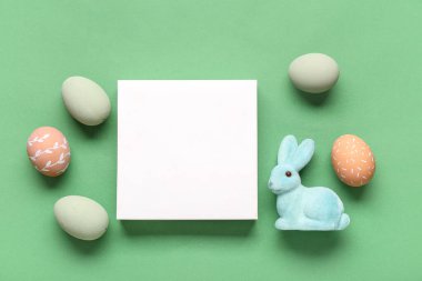 Boyalı yumurtalar, Paskalya tavşanı ve yeşil arka planda boş bir kart. Üst görünüm