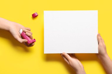 Sarı arka planda astım spreyi ve boş kartla çocuk elleri.