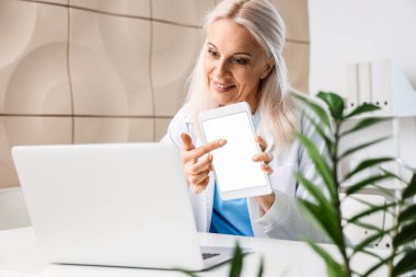 Olgun kadın doktor, ofisteki hastaya tablet bilgisayar gösteriyor.