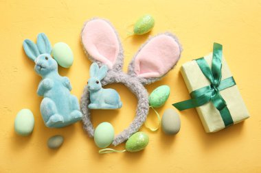 Paskalya yumurtalı tavşan kulakları ve sarı arka planda hediye kutuları.