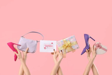Hediye kutuları, yüksek topuklu ayakkabıları ve pembe arka planda neşeli kartpostalları olan kadın elleri. Uluslararası Kadınlar Günü için Alışveriş