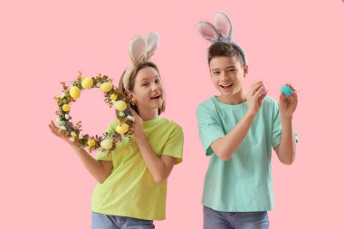 Paskalya yumurtası ve pembe arka planda çelengi olan tavşan kulaklı mutlu çocuklar.